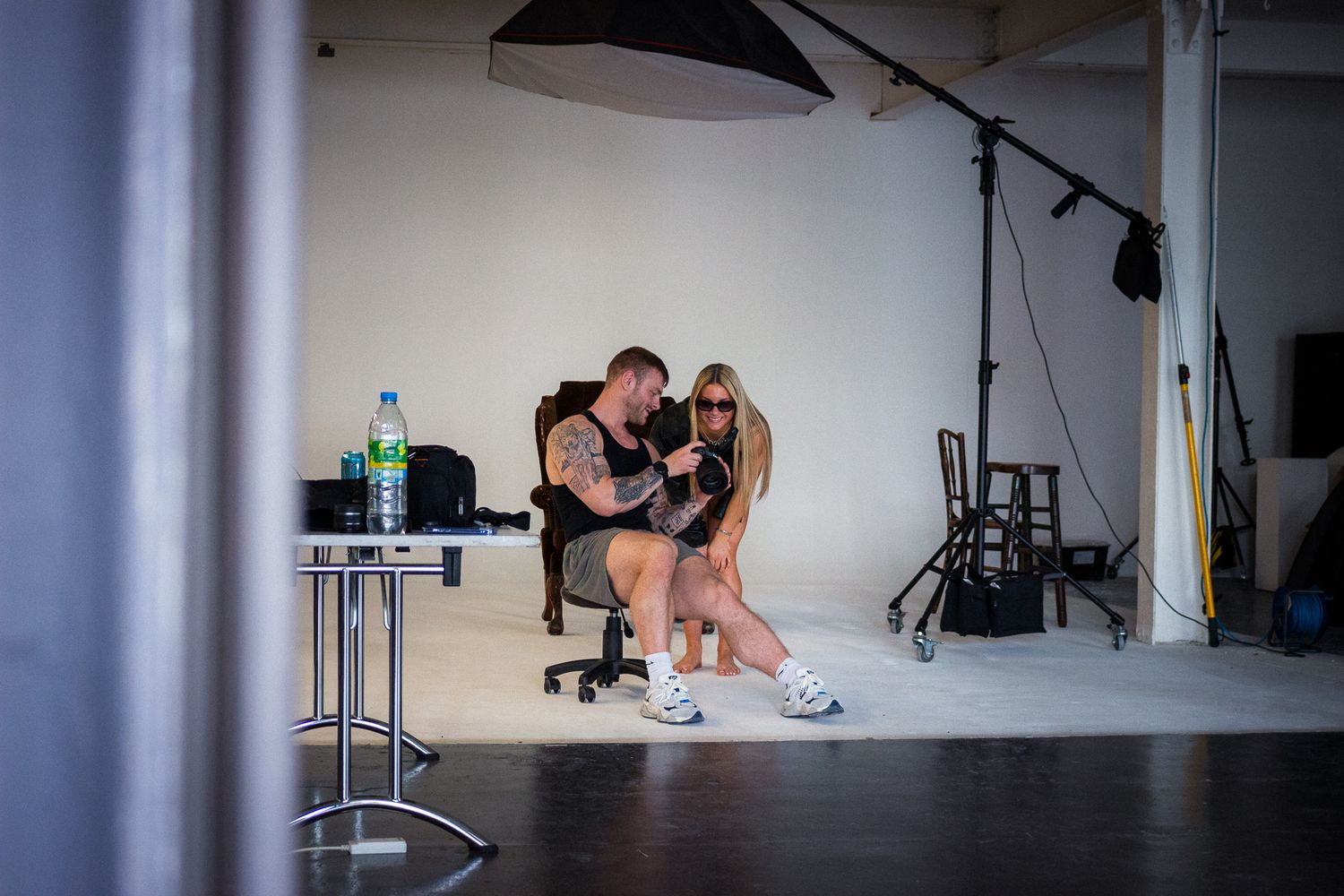 Behind-the-scenes photo of a photoshoot in a studio with lighting equipment and a small table with water bottle visible.