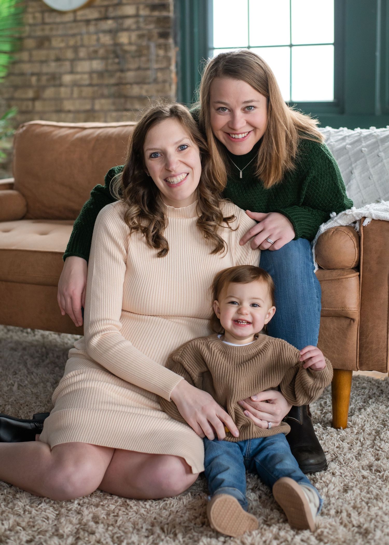 Family group sitting together on living room floor by brown leather couch in cozy home interior setting.