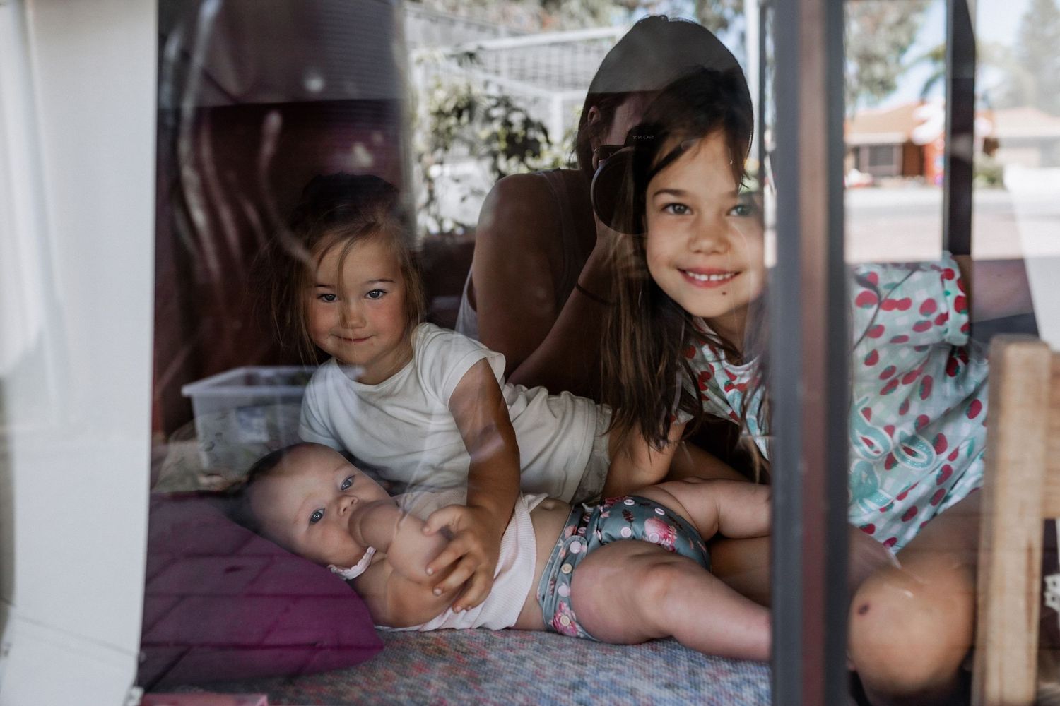 A window reflection of Bethany with her daughters at their home