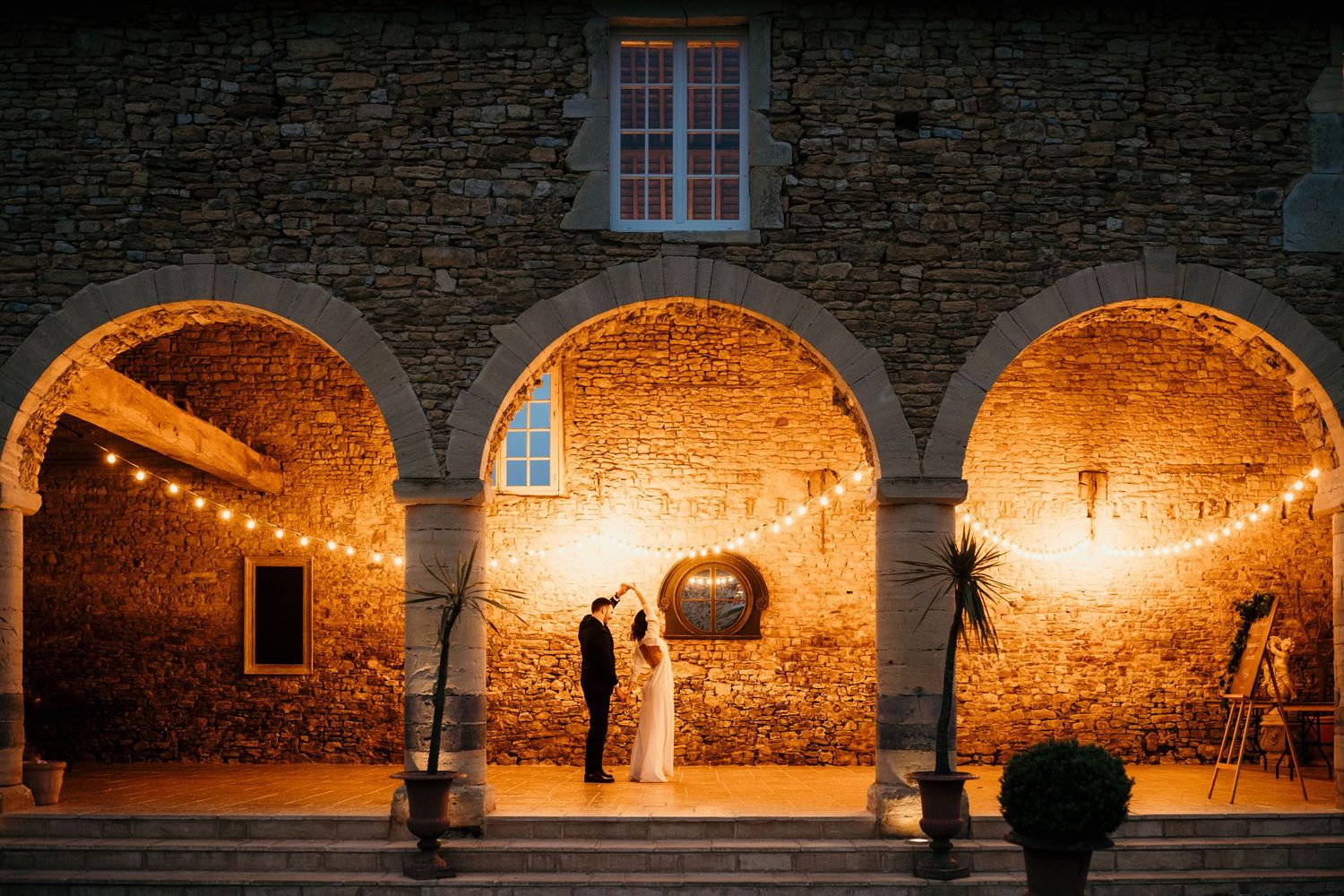An atmospheric wedding photo under illuminated stone arches with warm ambient lighting.