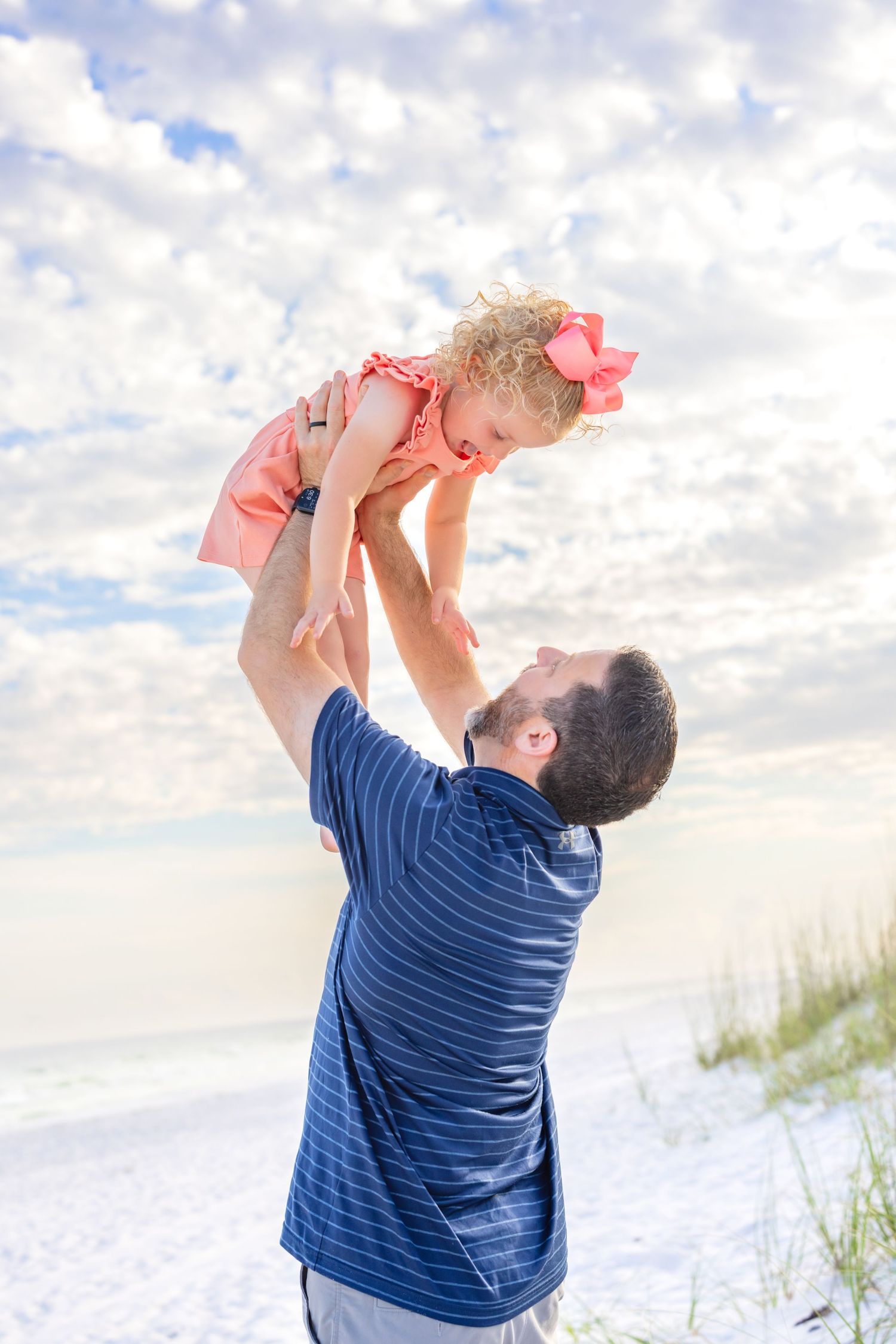 A family runs joyfully together along a white sandy beach at sunset beside turquoise ocean waves.