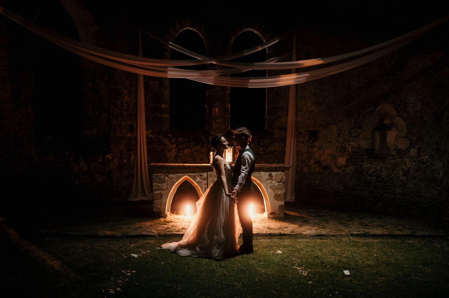 Silhouetted couple stands under wooden arch with dramatic night lighting.