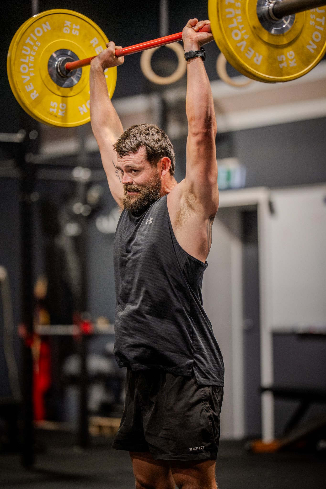 Athletic person performing an overhead barbell lift with yellow plates in a dark gym setting.
