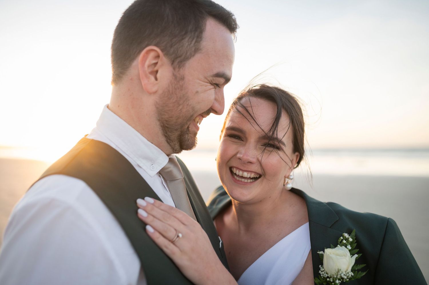Joyful wedding couple sharing intimate moment at sunset by the ocean.