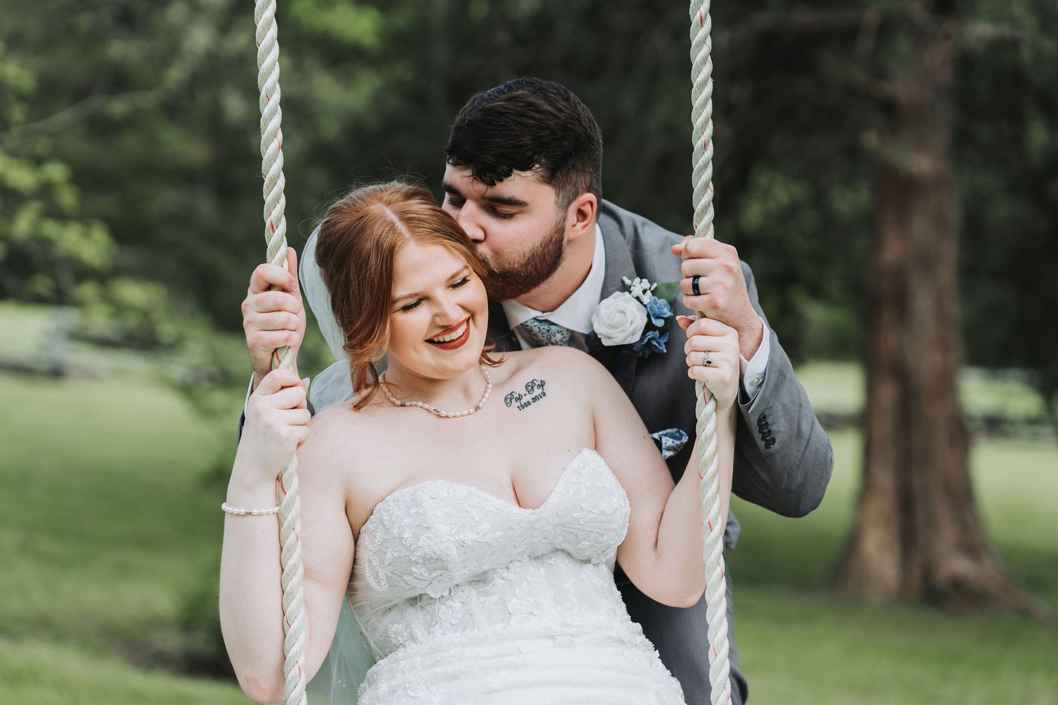 A couple share an intimate moment on a swing in a scenic outdoor garden setting.