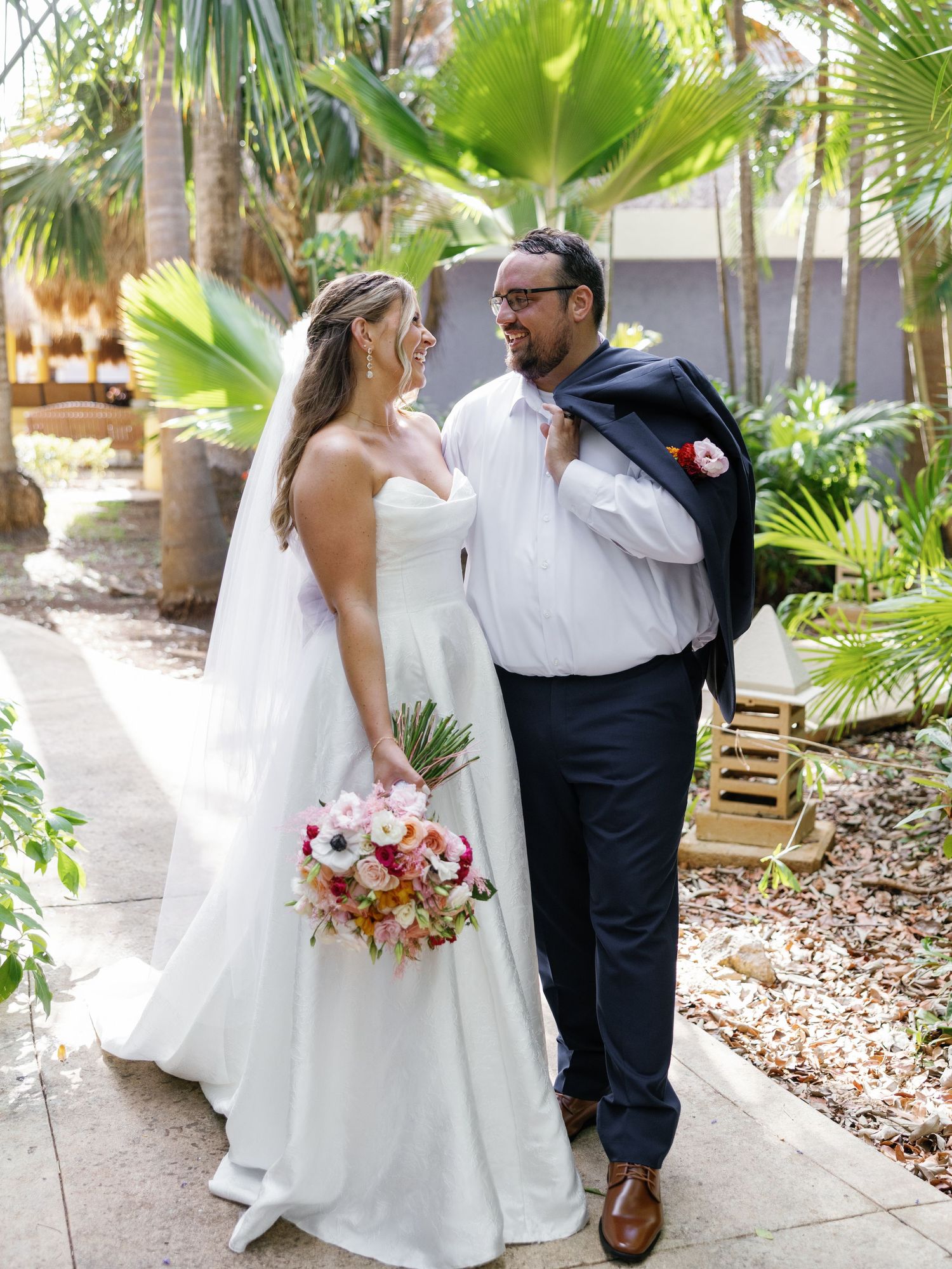 A couple shares an intimate moment in a tropical garden setting with palm trees and lush greenery.