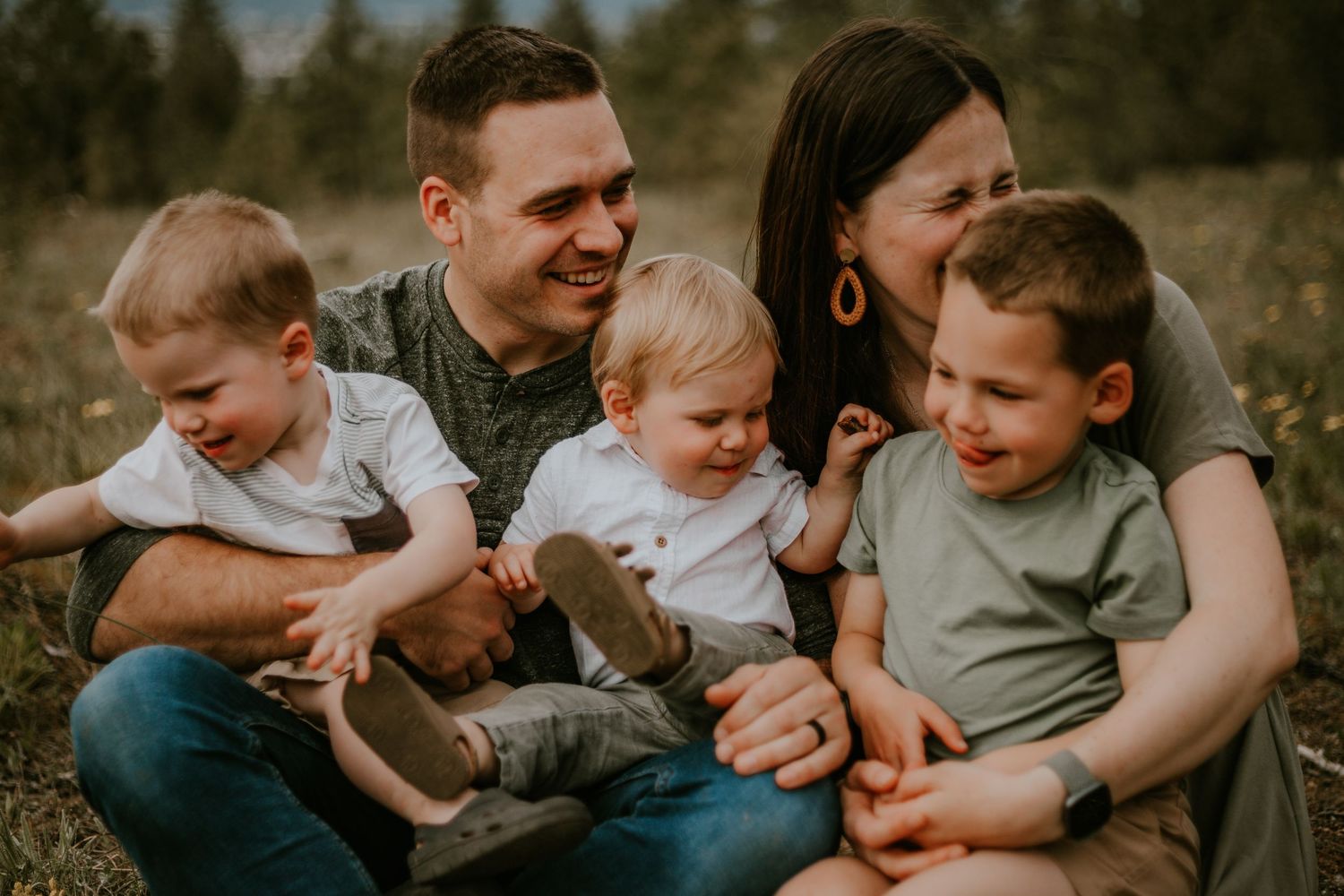 A family of five sits together outdoors sharing a candid moment in warm sunset lighting.