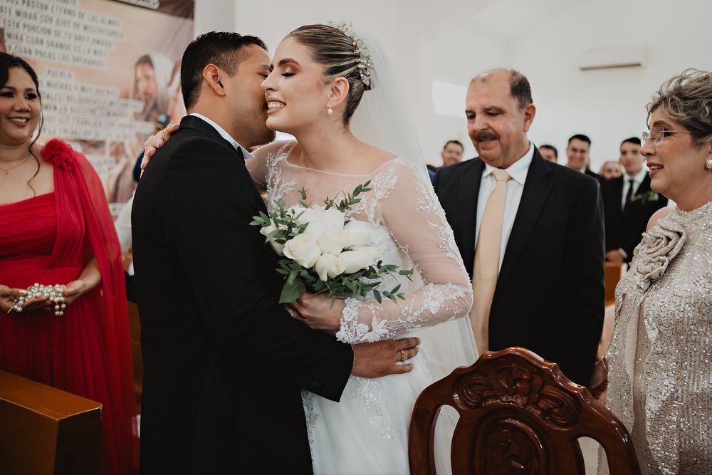 A couple shares an intimate kiss during their wedding ceremony in a light-filled venue.