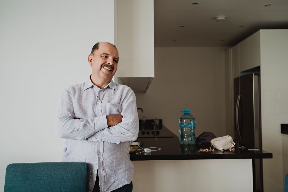 Someone stands casually in a modern kitchen interior with stainless steel appliances and dark countertops.