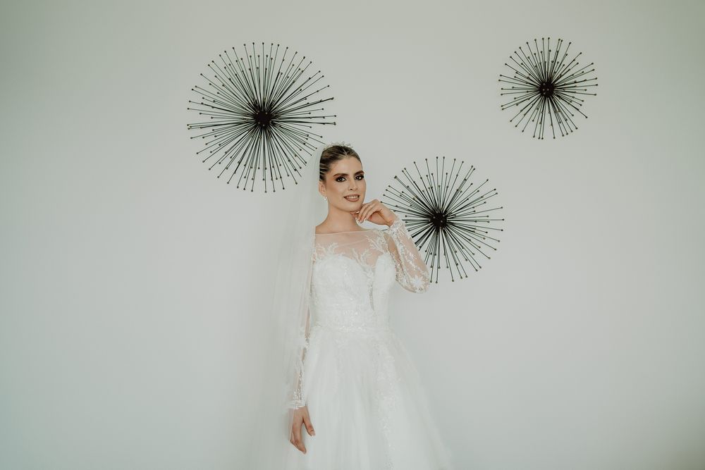 A bride in a lace wedding dress poses in front of decorative starburst wall art.