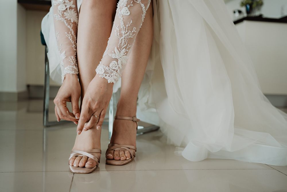 Close-up view of beige high heels with crystal embellishments next to white tulle fabric.