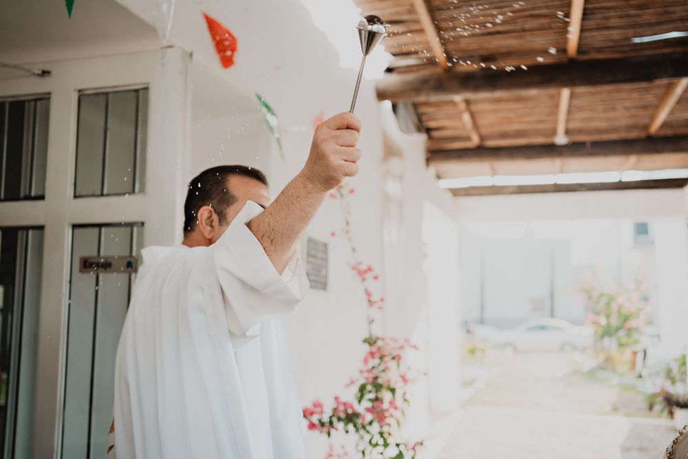 A couple in white wedding attire embraces during a romantic outdoor ceremony with natural light streaming through.