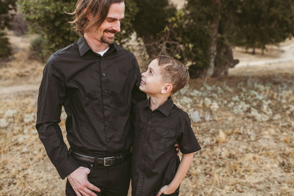 A father and son share a joyful moment together while wearing matching black button-up shirts outdoors.