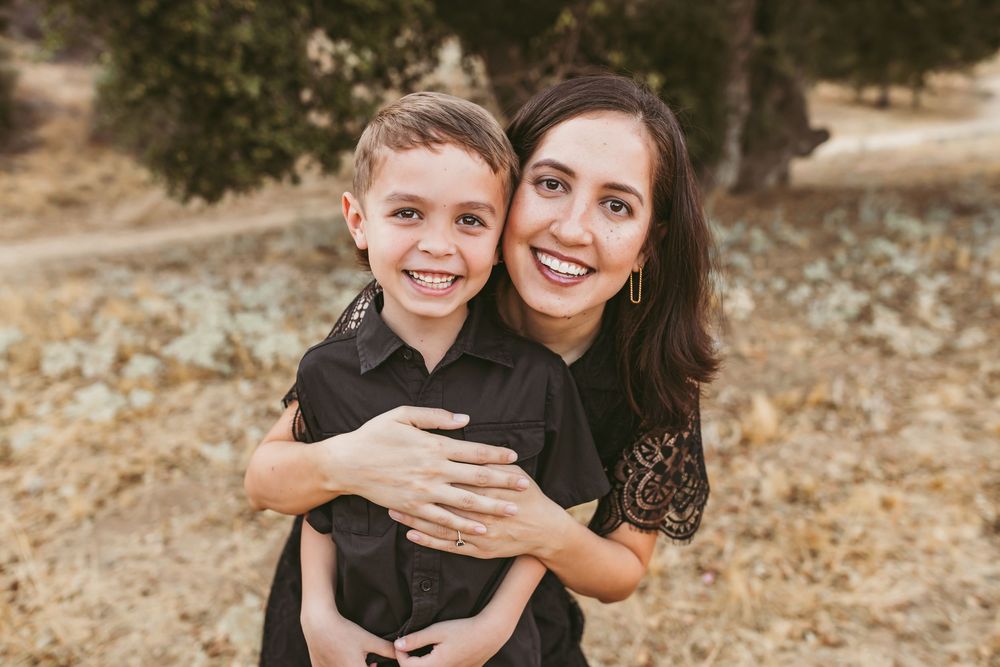 A mother and son share a warm embrace while posing for a portrait in an outdoor setting.