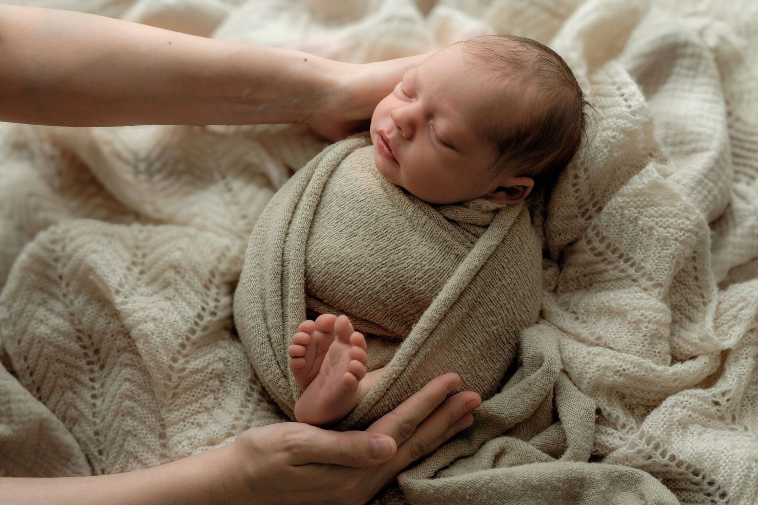 Sleepy newborn swaddled in blanket in parents arms