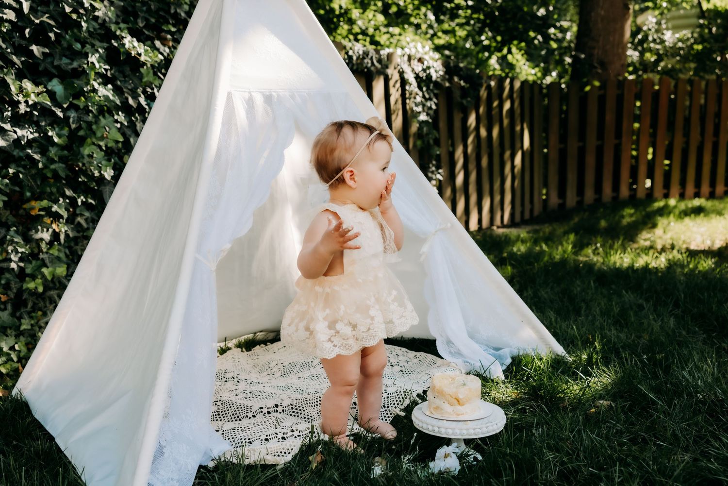 Wedding dress hanging in sunlit garden with teepee tent setup and romantic natural outdoor decor for special celebration.