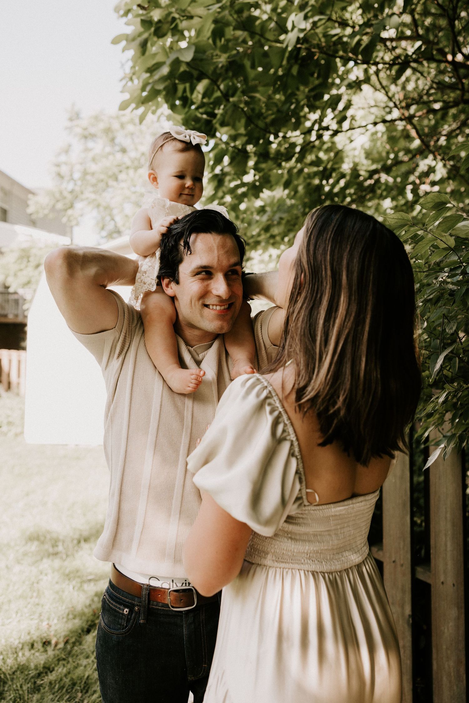 A loving family moment outdoors in a garden, with light warm tones and greenery creating a peaceful summer atmosphere.