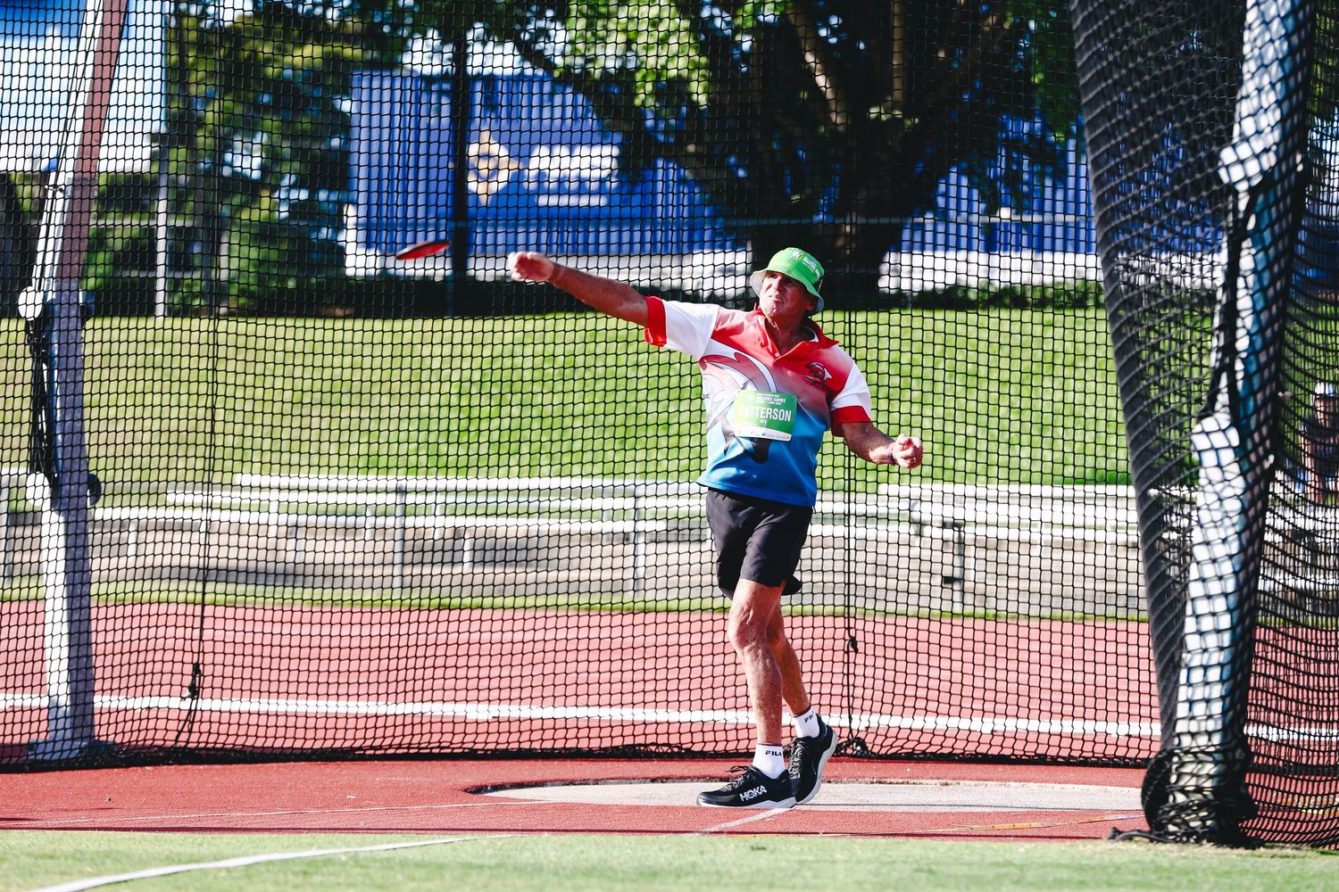 Athlete in action performing a discus throw at an outdoor track and field facility on a sunny day.