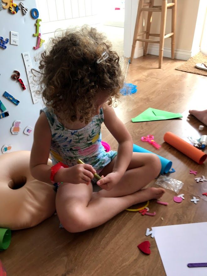 A child sits on a hardwood floor while engaged in arts and crafts activities with colorful paper and supplies.