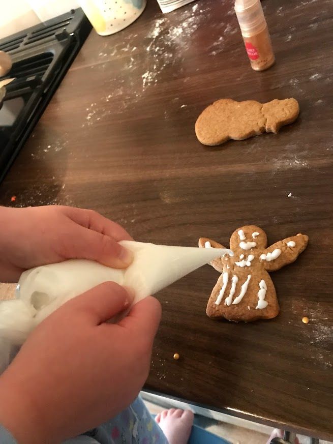 A sequence of photos showing hands decorating gingerbread cookies with white icing on a dark wooden surface.