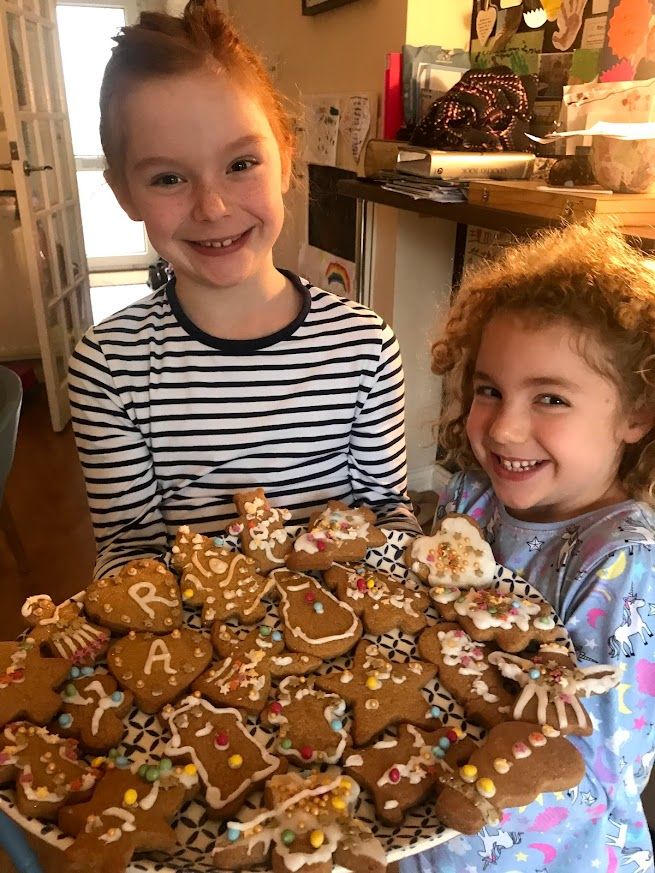 Two children in striped shirts smile while decorating homemade gingerbread cookies with white icing for the holidays.