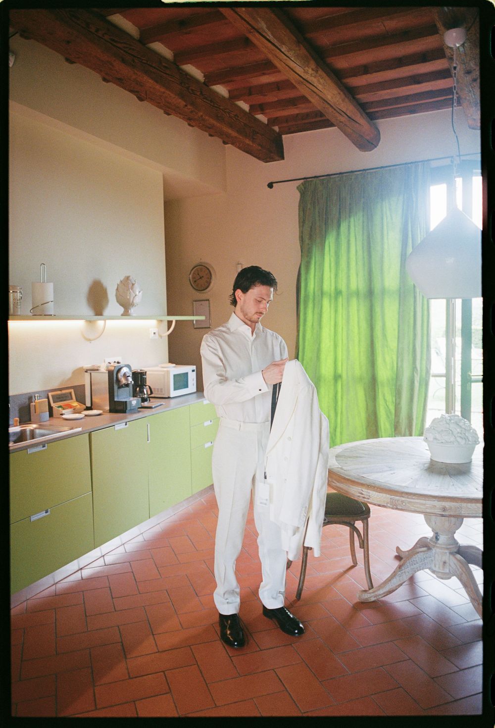 Interior of a rustic Tuscan kitchen with wooden beams and green curtains.
