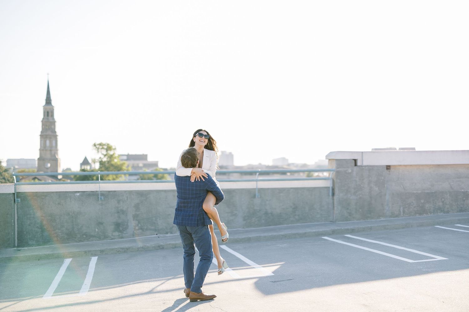 Person walking along a narrow rooftop ledge in an urban setting, casting long shadows in bright sunlight.