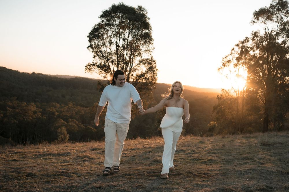 A couple walking hand in hand on a hilltop at sunset with eucalyptus trees silhouetted in the golden light.