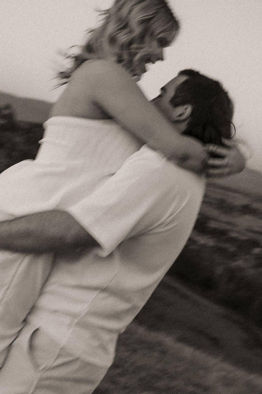 A romantic black and white photo shows a couple embracing in an intimate moment outdoors.