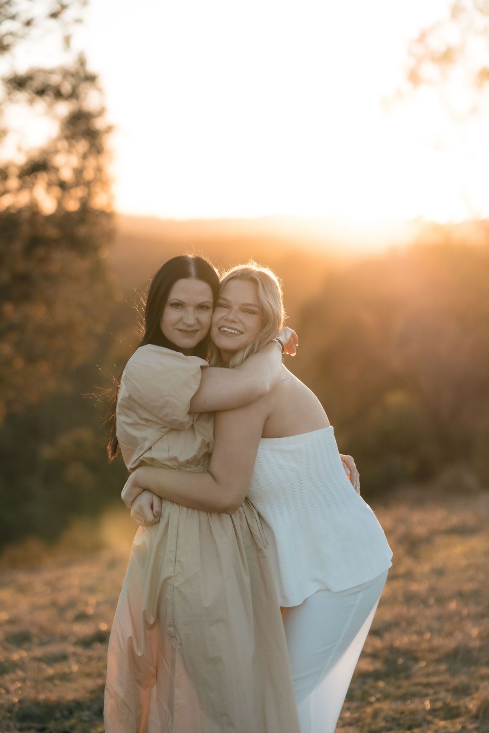 Two people hugging and laughing together in a sun-drenched field at sunset.