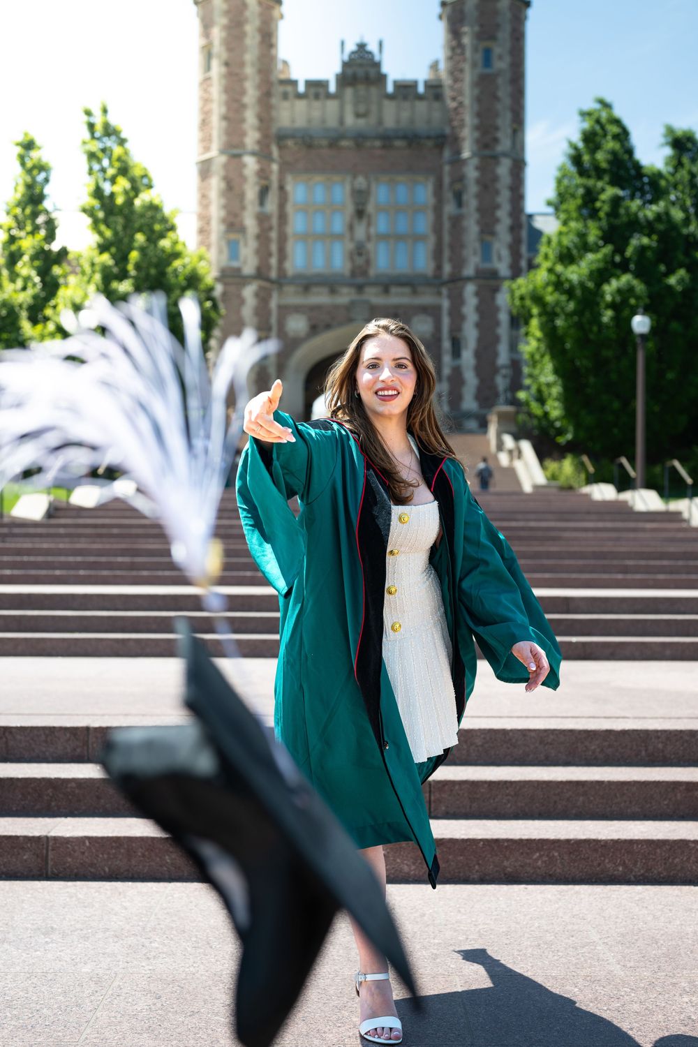 Graduate tosses cap in celebration on stone steps of historic university building.