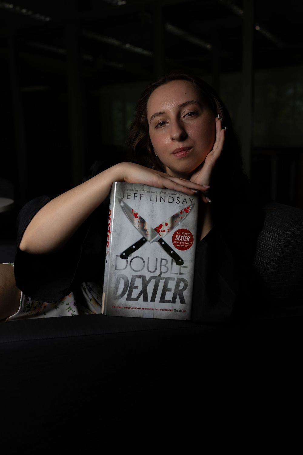 Woman posing with Jeff Lindsay's Double Dexter book in dramatic dark lighting, resting her chin on her hand.