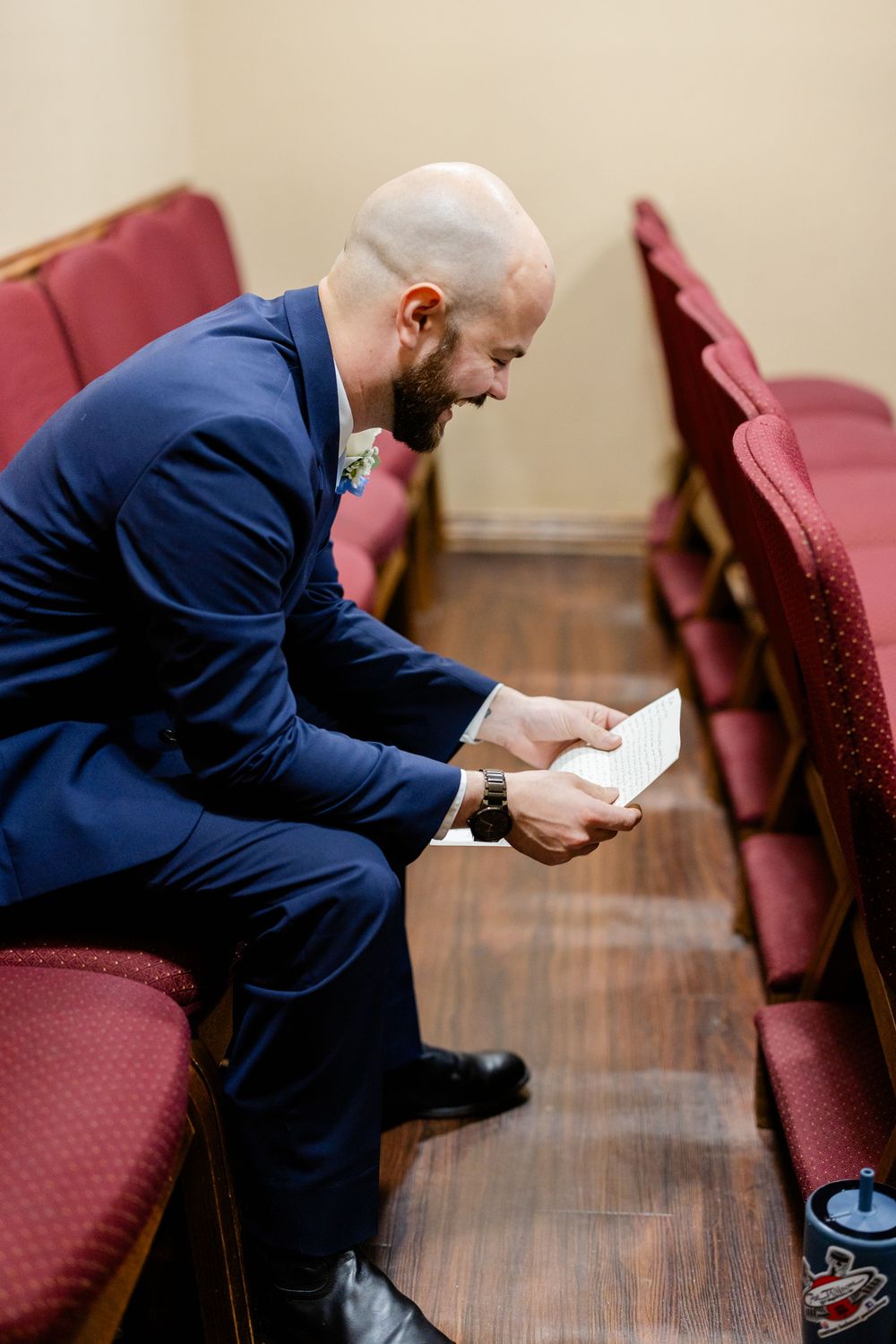 A person in a navy suit sits alone in a church pew reading a document during a quiet moment.