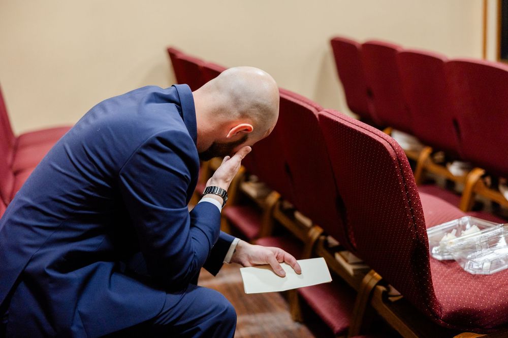 A person in a blue suit sits alone in church pews while reading from a book.