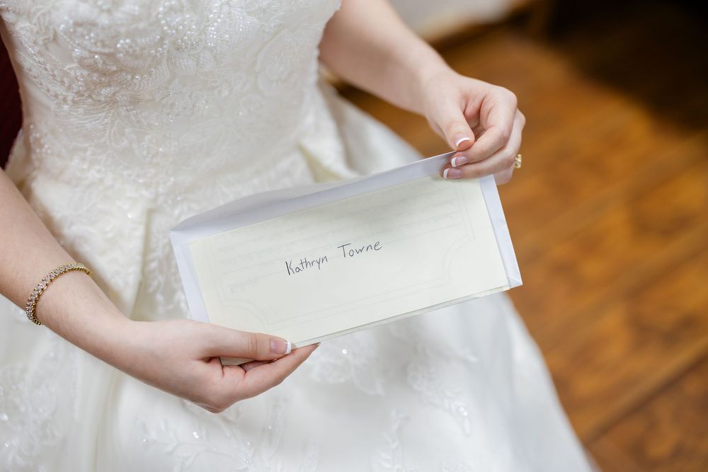 Close up of hands holding an elegant white envelope on a lace wedding dress.