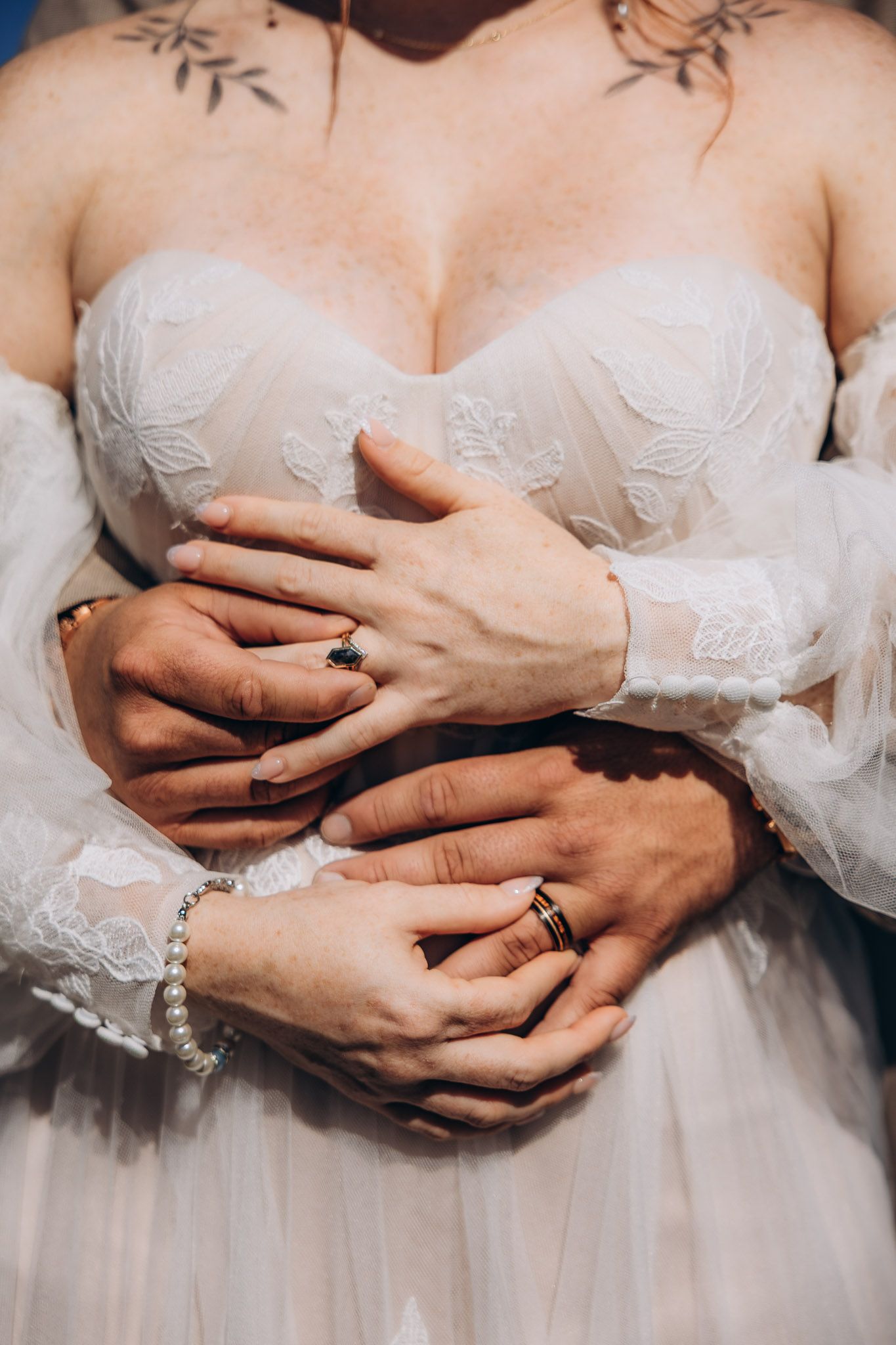 Close up view of hands with wedding rings and bracelet holding onto white lace wedding dress bodice.