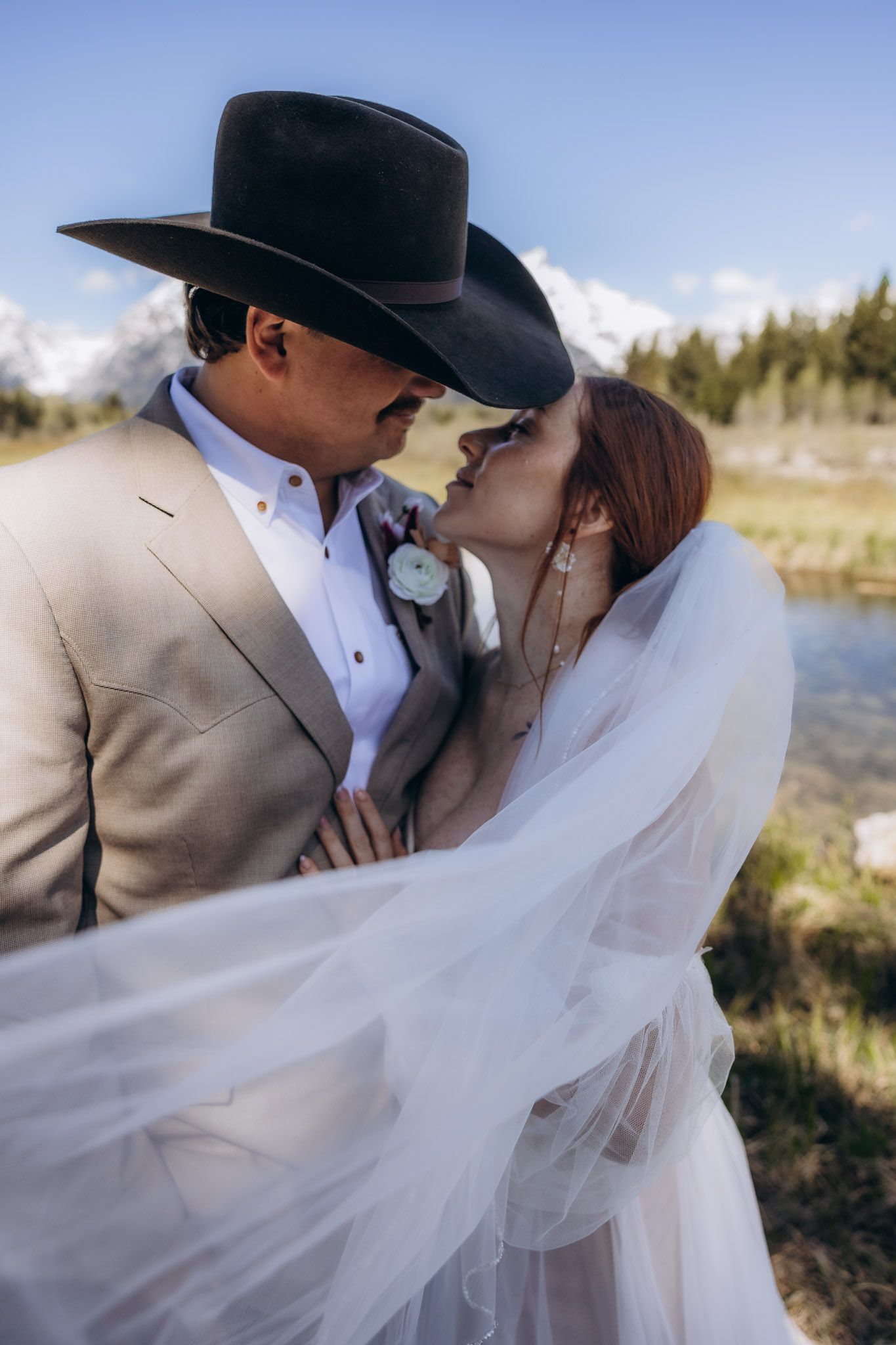 Romantic couple sharing an intimate moment during their western-themed wedding photoshoot by a lake.