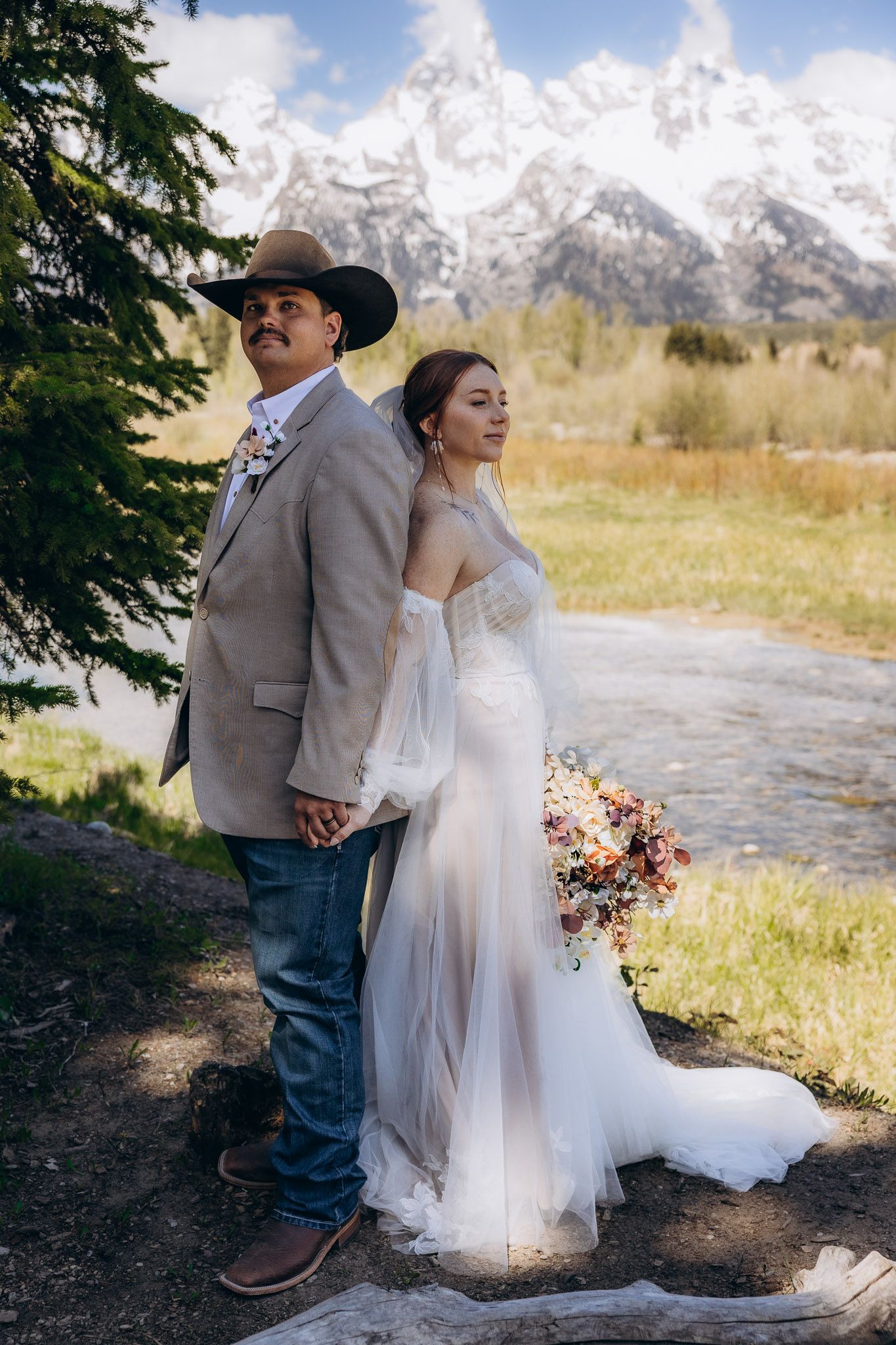 Western style wedding portrait with couple standing back-to-back by mountain stream.