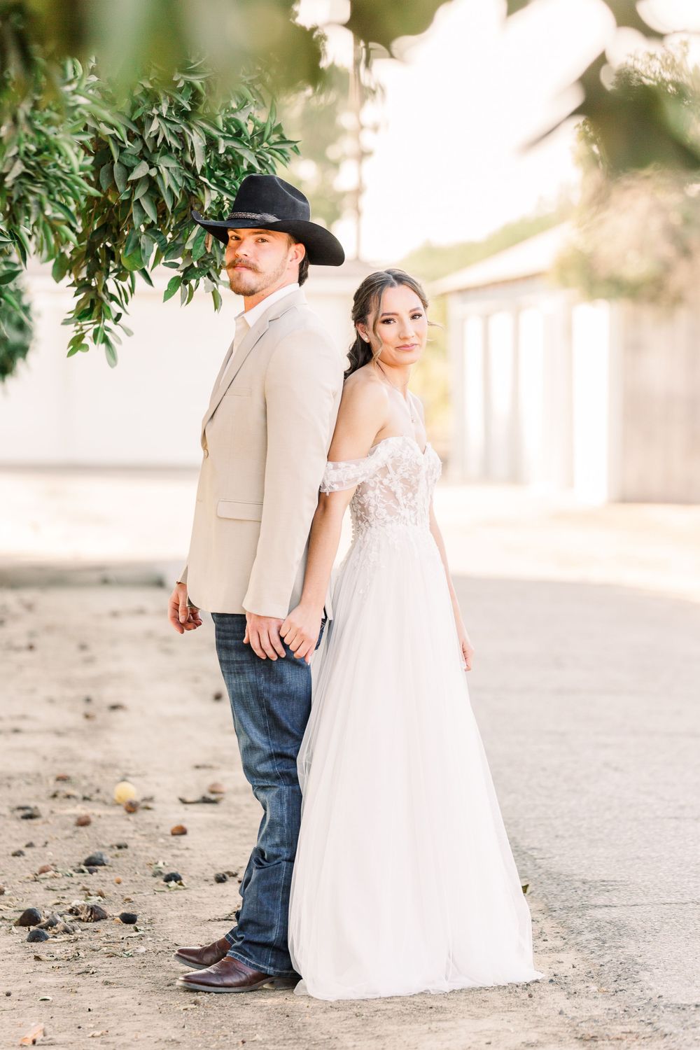 A couple poses back-to-back outdoors, combining western and elegant wedding styles.
