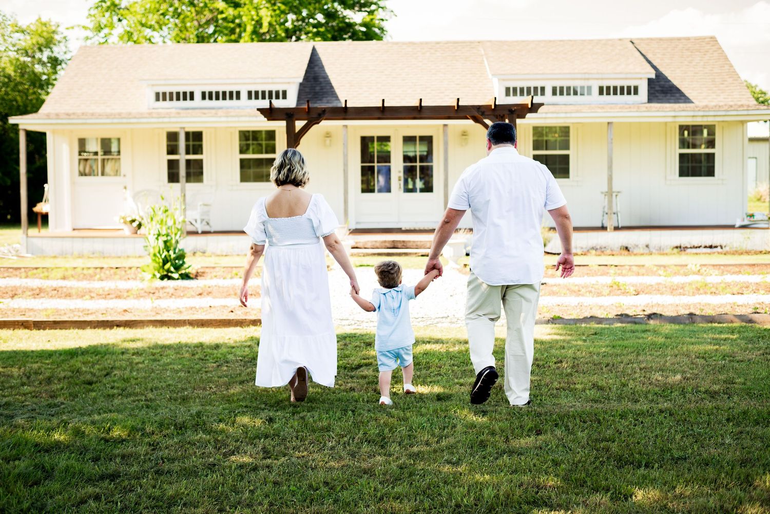 Back view of couple walking on grass with small child between them holding hands.