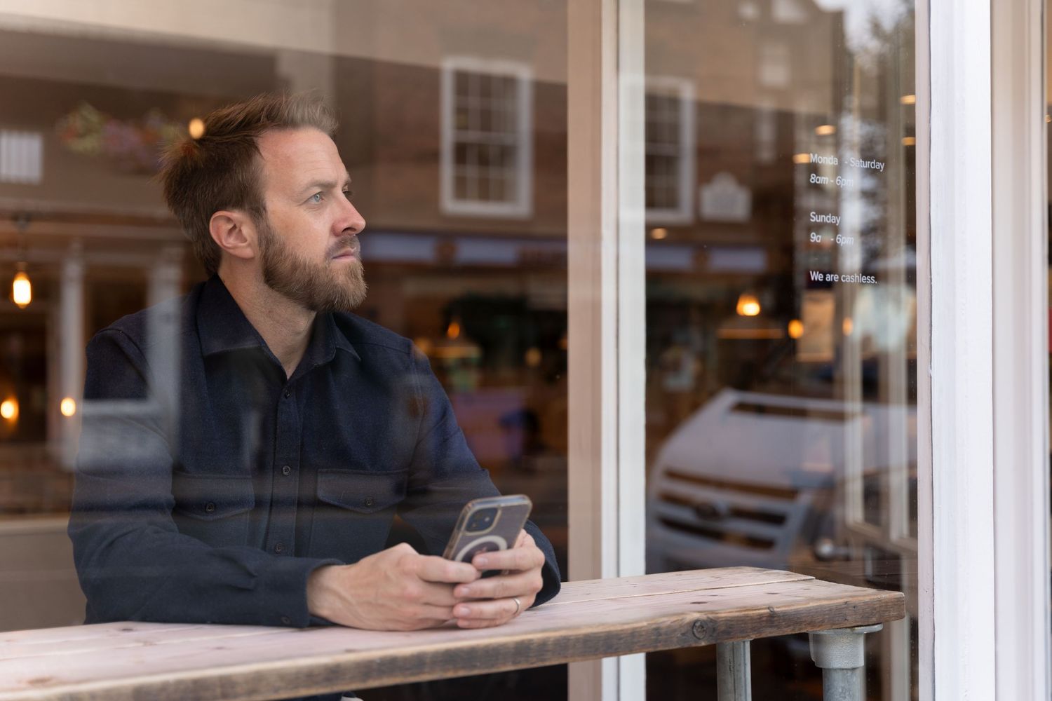Life coach looks out of a window as a personal branding photographer takes his photo through the glass showing some reflections.