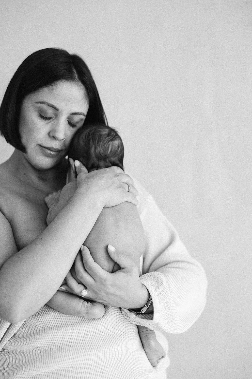 A tender black and white portrait of a mother cradling her newborn baby in a gentle embrace.