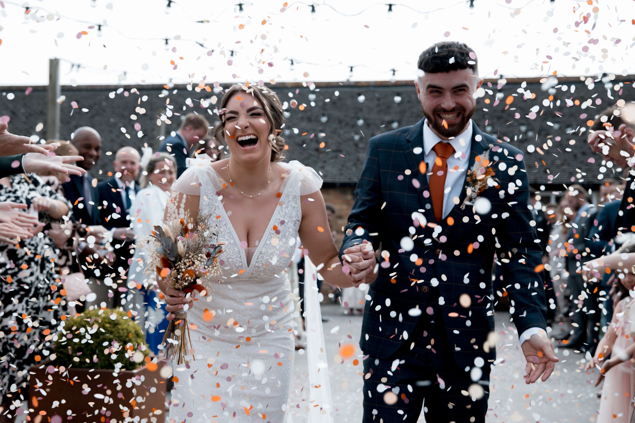 Joyful wedding celebration with confetti flying through the air against a dark background.