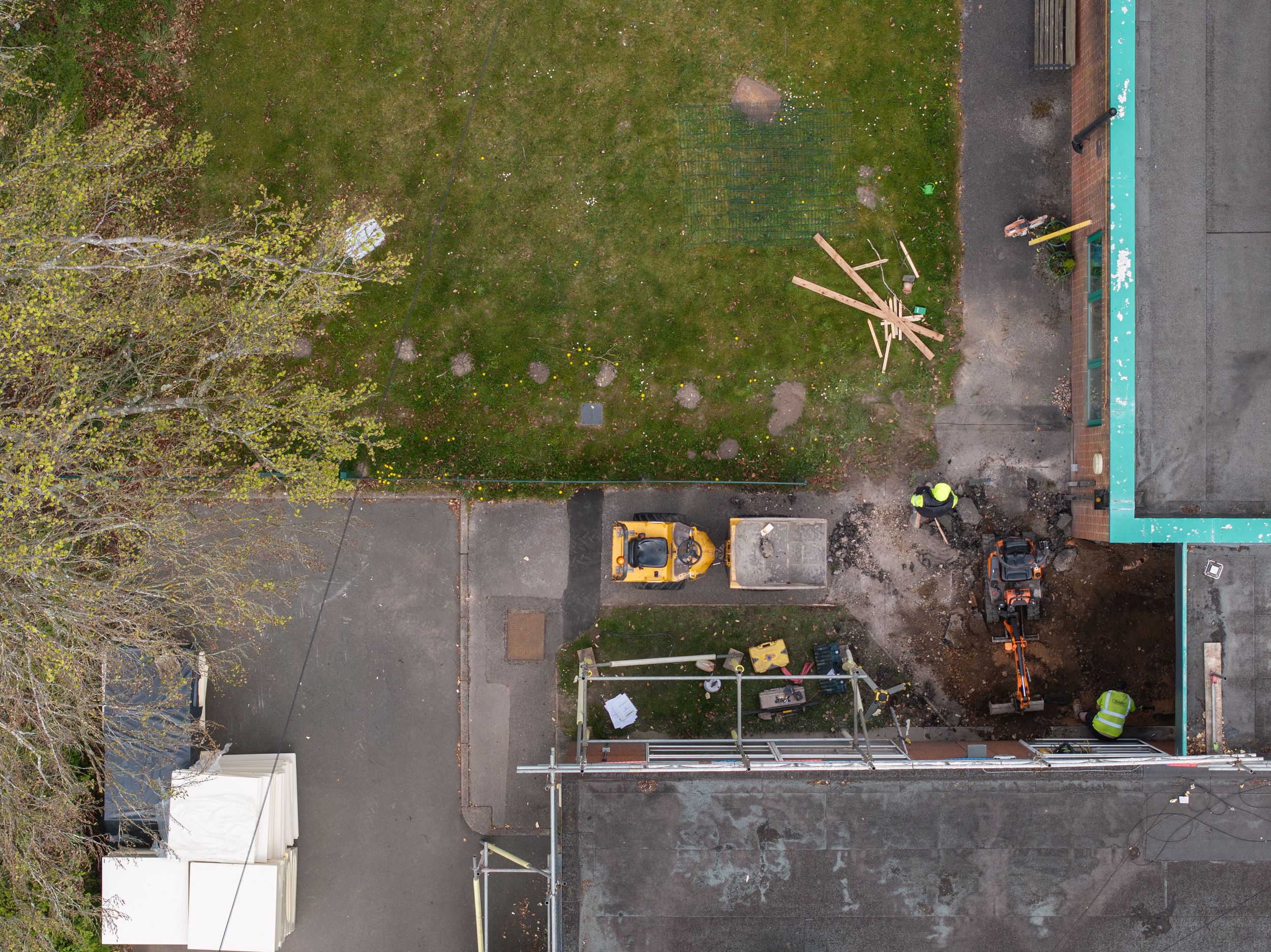 Bird's eye view of building rooftop with scattered equipment, grass area, and trees along the edge.