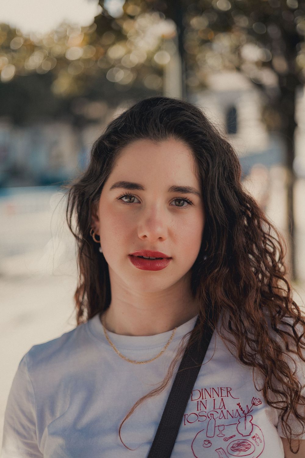 Portrait shot with curly hair against blurred bokeh background wearing white graphic tee.