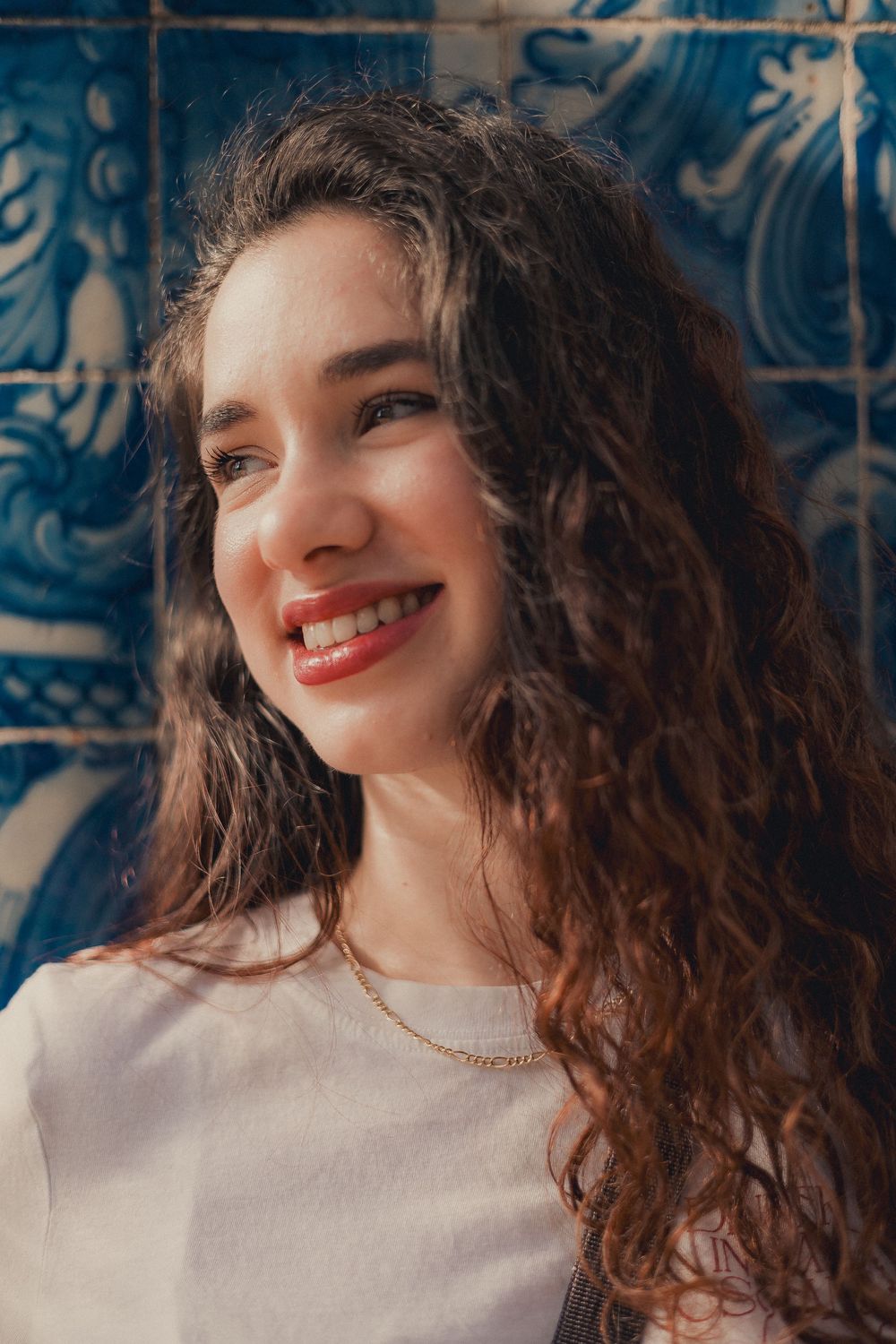 Portrait against blue tiled wall showing curly hair and bright smile.