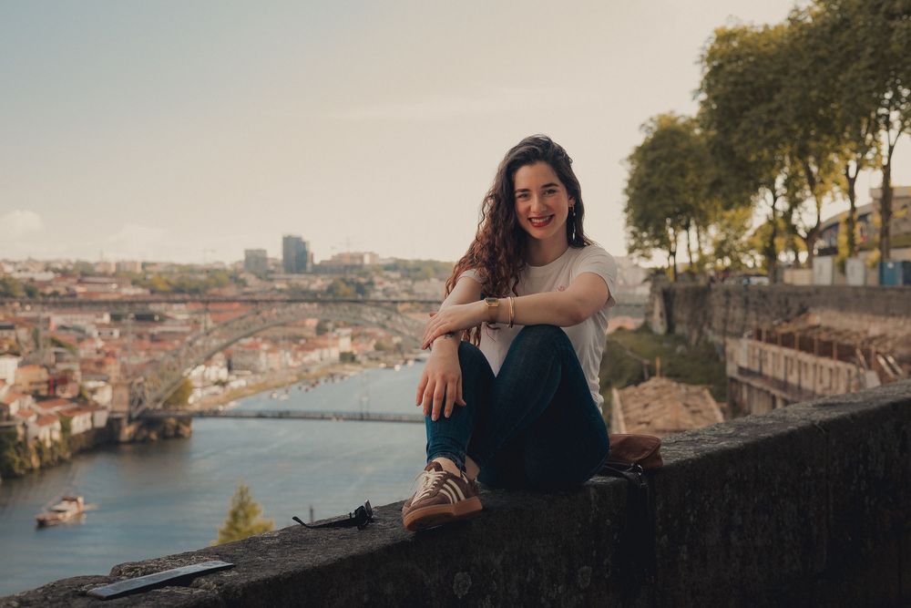Relaxed portrait sitting on stone wall overlooking Porto's river landscape.