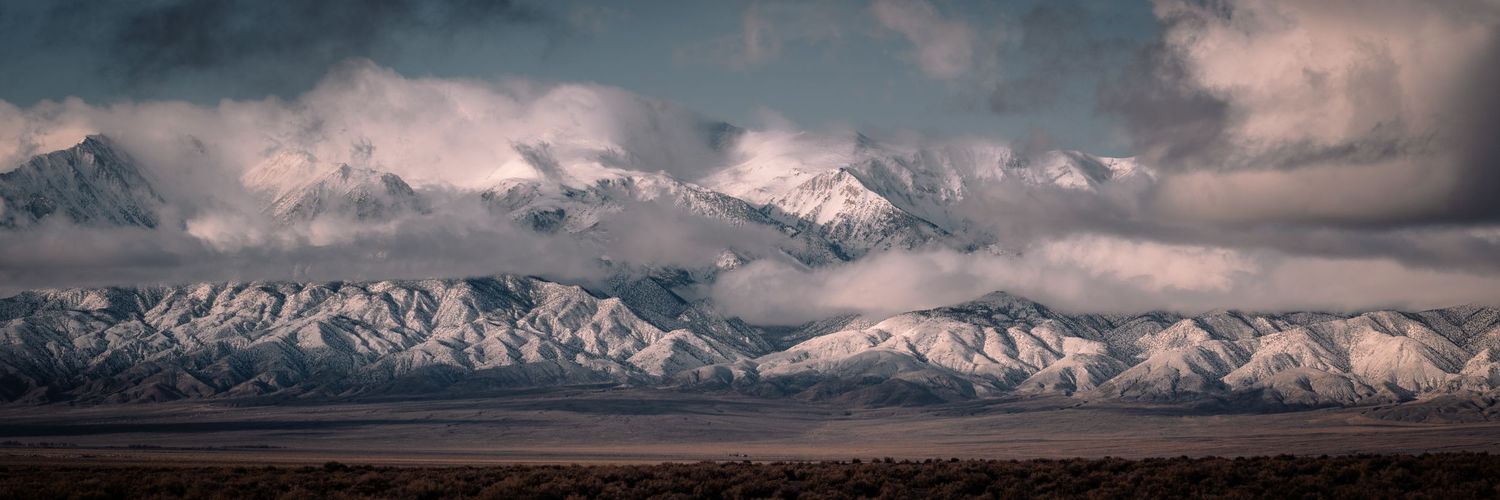 Dramatic panoramic view of snow-covered mountain range beneath billowing storm clouds.