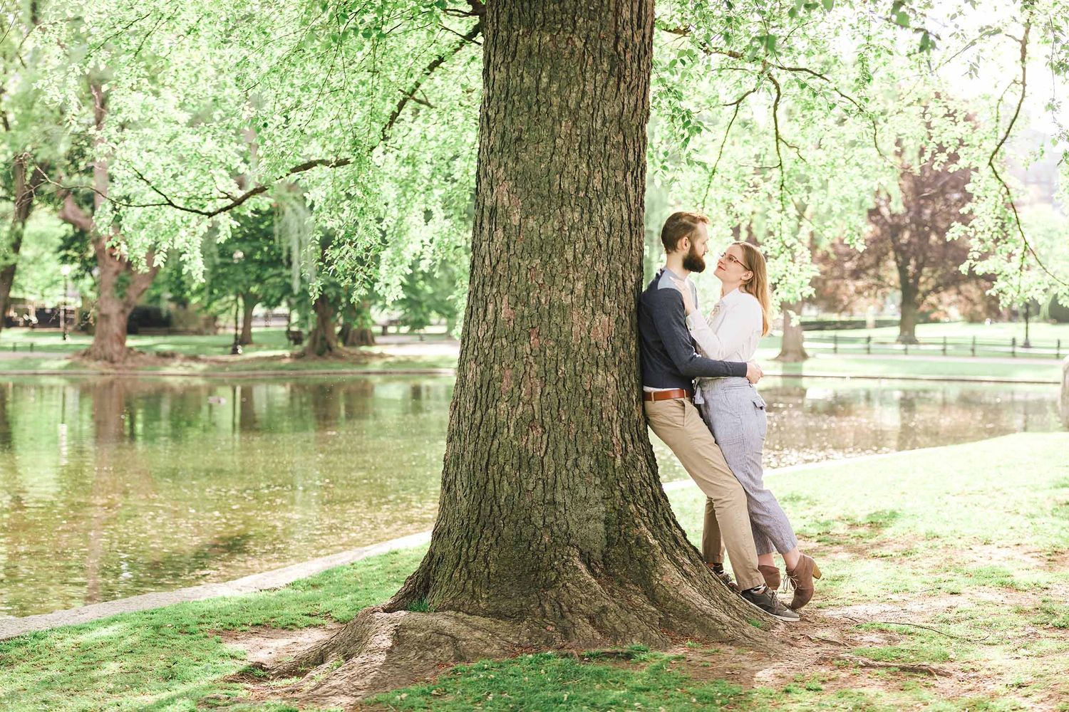 Intimate portrait of couple leaning against tree beside Lagoon in Boston Public Garden, with reflections in the background