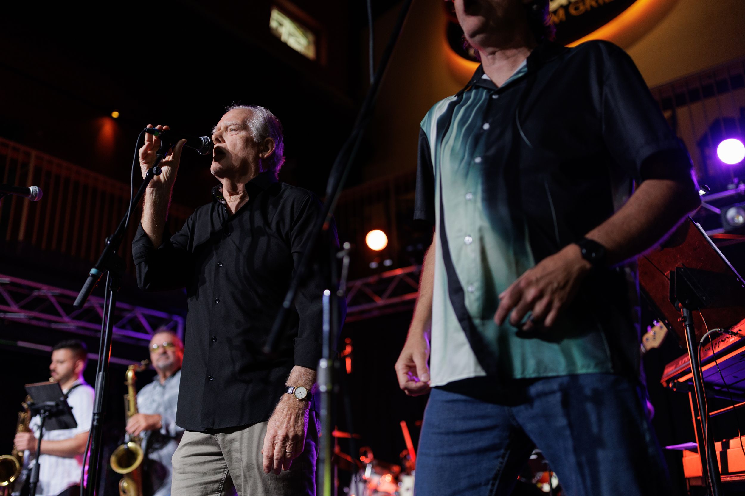 Musicians performing on stage with stage lighting and microphones at a concert venue.